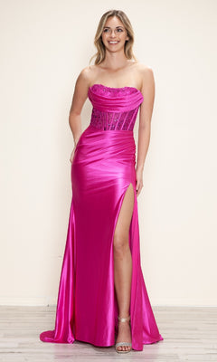 A woman with blonde hair smiles indoors in the Strapless Long Corset Prom Gown: Poly USA 9688, a bright pink satin dress with a sheer lace corset bodice and high slit.