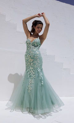 A woman in the Sequin-Floral Long Mermaid Prom Dress: Eureka 9696 stands outdoors against a white textured wall, raising her arms and smiling.