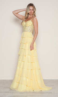 A woman in a yellow Long Tiered Corset Prom Dress (Poly USA 9698) with a lace corset-style bodice stands against a plain light background.