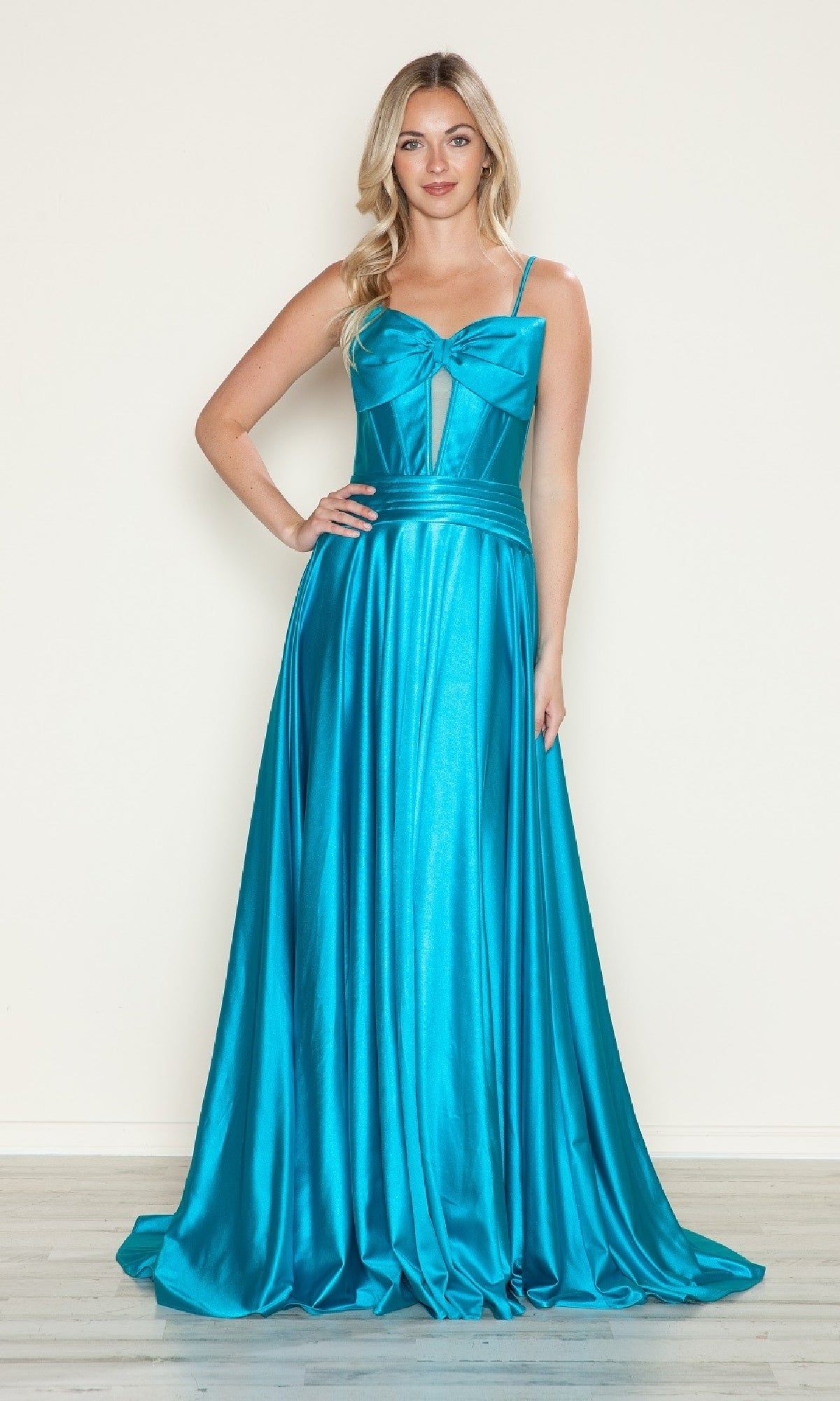 A woman poses against a plain wall in the Bow-Front Long Corset Prom Dress (Poly USA 9702), a shiny turquoise evening gown featuring thin straps, a bow detail on the bodice, and a floor-length silhouette.