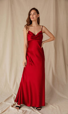 A woman in the Eureka 9711 Cowl-Neck Long Satin Prom Dress stands against a beige fabric backdrop, gazing slightly to her left.