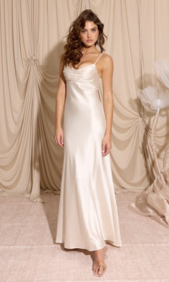 A woman stands on a beige carpet in front of ruched drapery, wearing the Eureka 9711 Cowl-Neck Long Satin Prom Dress with thin straps and a soft cowl neckline.
