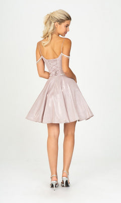 A woman faces away in the Eureka 9722 short prom dress, a light pink glitter-jersey cocktail dress with a flared skirt, off-the-shoulder jeweled chains, and white heels, set against a plain white background.