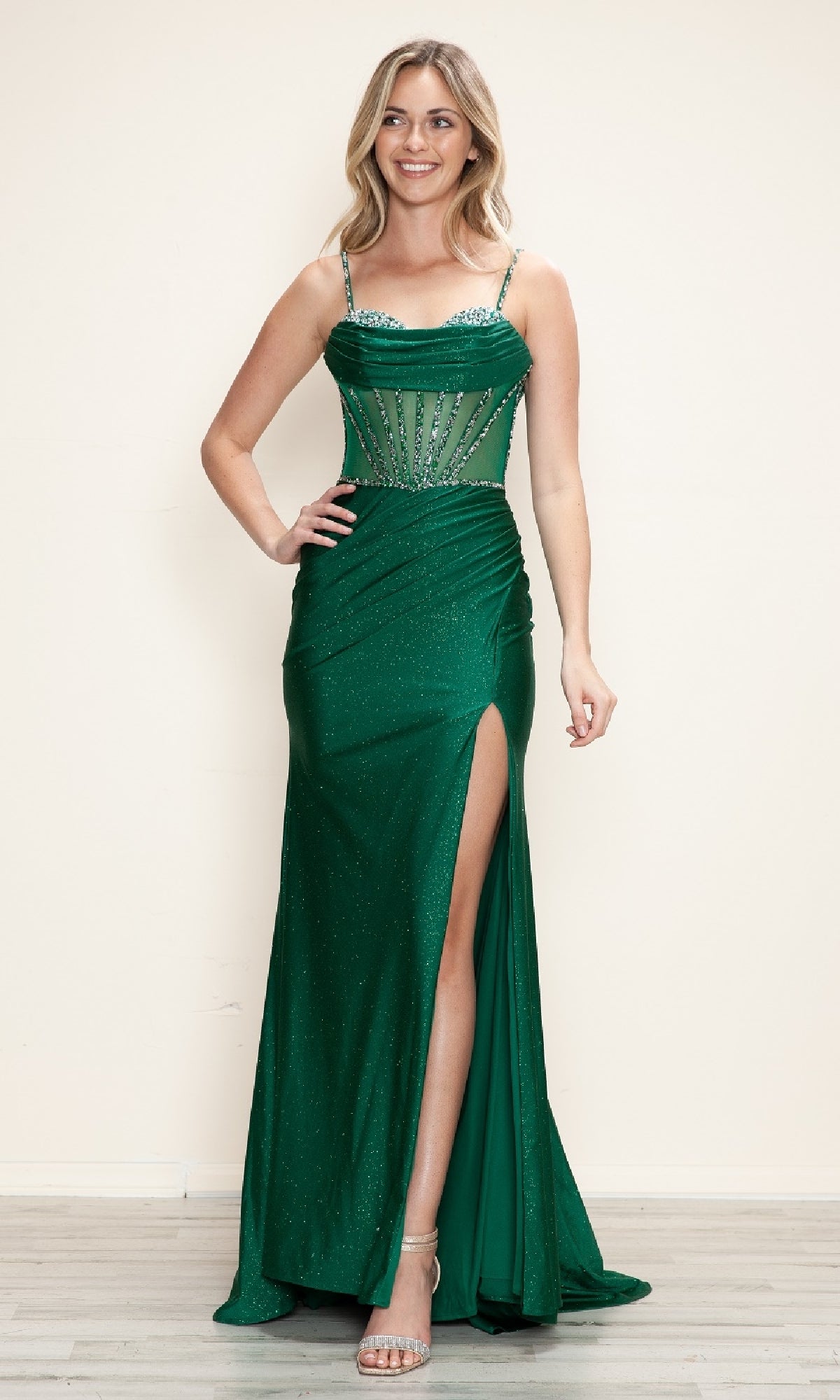 A woman stands indoors, smiling at the camera in the Sheer Beaded-Corset Long Prom Dress: Poly USA 9750, featuring a high slit and sheer beaded bodice.