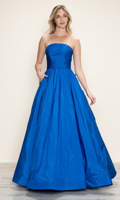 A woman in the Long Prom Dress: Poly USA 9754, featuring a strapless ruched bodice and floor-length bright blue taffeta skirt with an adjustable lace-up back, stands on a wooden floor against a plain light background.
