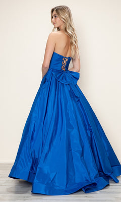 Woman wearing the Poly USA 9754 long prom dress with a strapless ruched taffeta bodice, large bow, and adjustable lace-up back, standing against a plain light-colored wall.