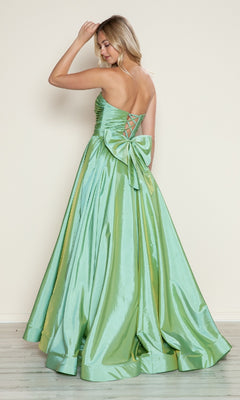Wearing the Poly USA 9754 long prom dress, a woman stands facing away, touching her hair. The shiny light green taffeta gown features a strapless ruched bodice, adjustable lace-up back, and a large accent bow enhancing her elegant style.
