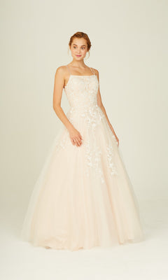 A woman wears the Eureka CC0240 Lace-Up Long Lace Prom Ball Gown in light pink with thin straps and delicate lace details, standing against a plain background.