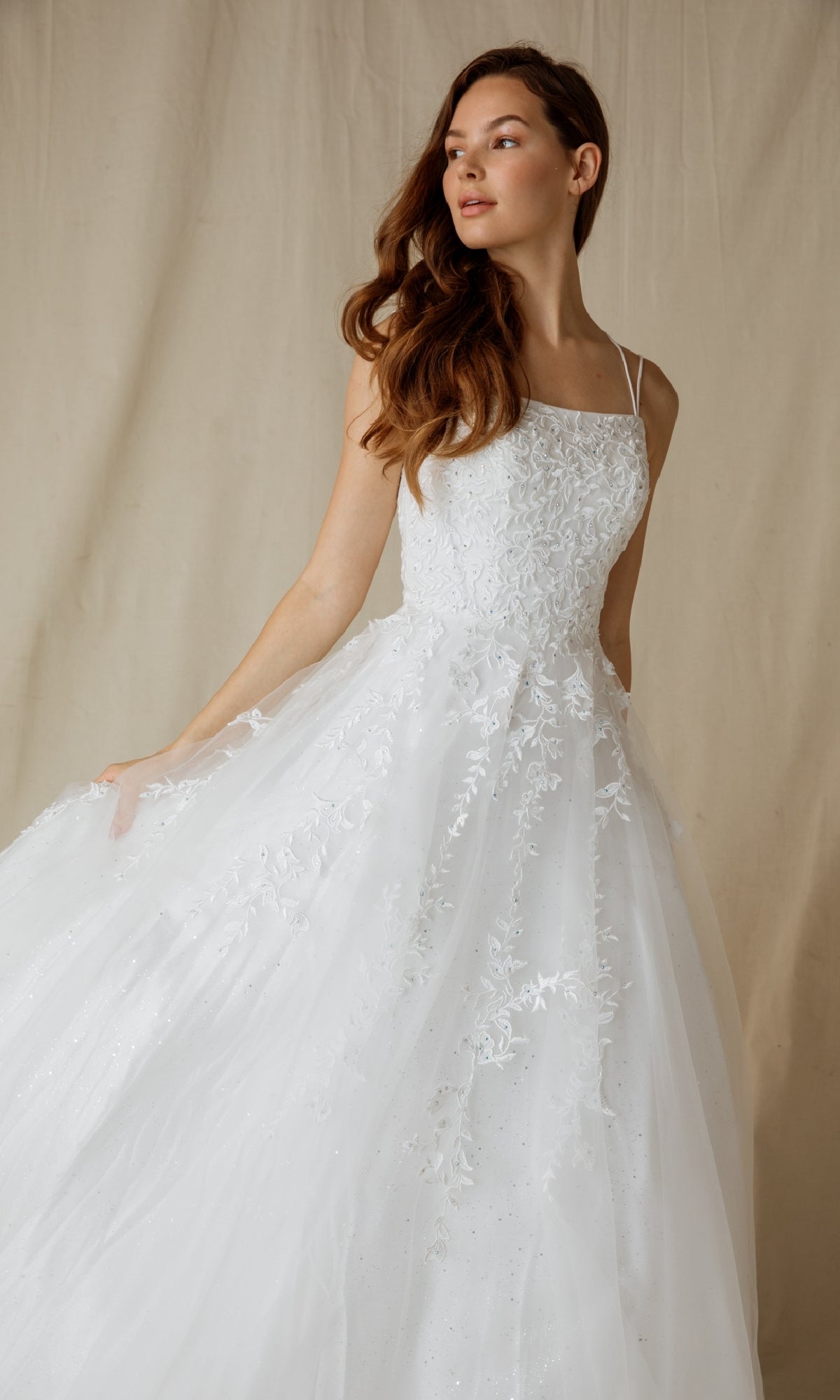 A woman wearing the Eureka CC0240 Lace-Up Long Lace Prom Ball Gown stands against a plain beige background.