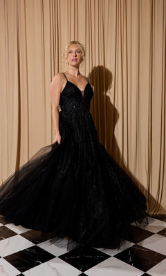 A woman wearing the Lace-Up Long Shimmer Prom Dress: Eureka 9797 in black stands on a black and white tiled floor before beige curtains.