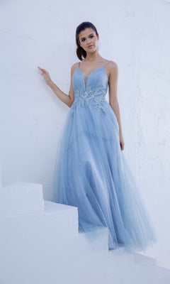 A woman in the Lace-Up Long Shimmer Prom Dress: Eureka 9797, a light blue floor-length A-line gown with a deep V neckline, stands on white stairs against a textured white wall.