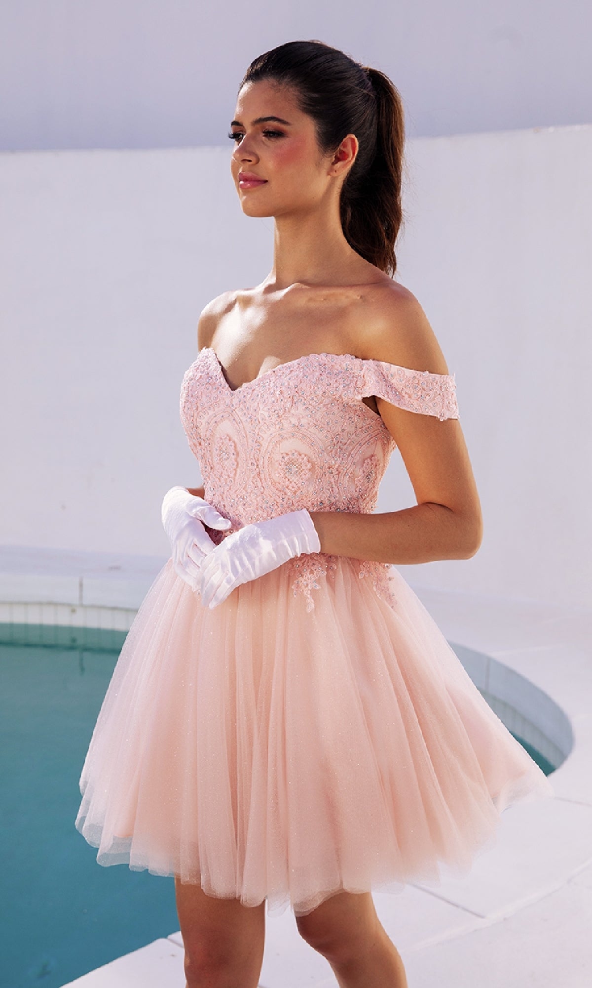 A woman wearing the Eureka 9833 off-the-shoulder short hoco dress and white gloves stands by a pool with a white background.
