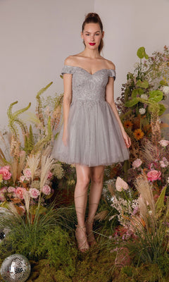 A woman stands on grass, surrounded by flowers, greenery, and two disco balls, wearing the Eureka 9833 Off-the-Shoulder Short Hoco Dress in light gray.