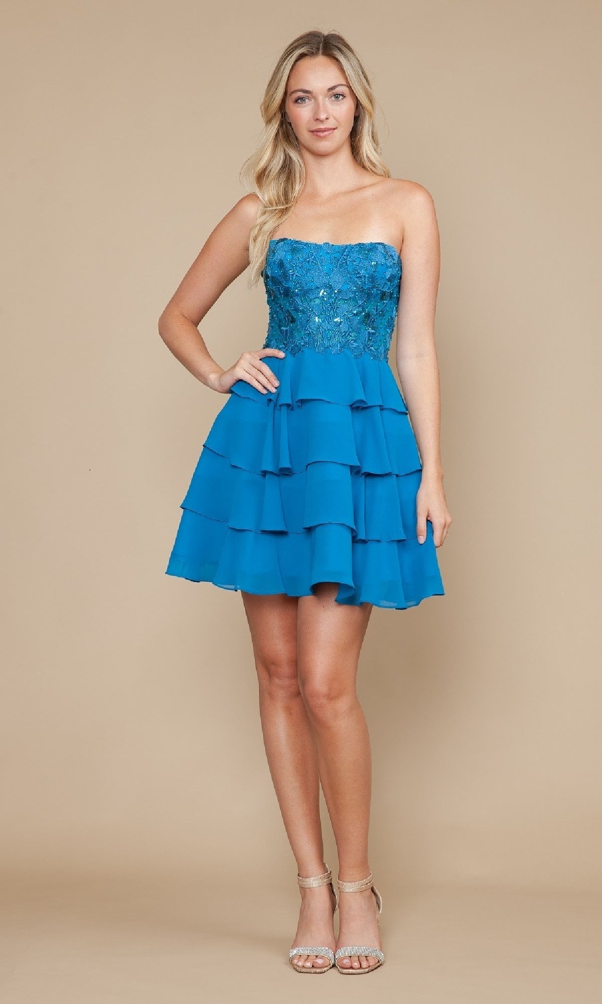 Model showcases the Strapless Short Ruffled Hoco Dress: Poly USA 9838, featuring a sequined corset-style bodice and tiered skirt, styled with strappy heeled sandals against a beige background.
