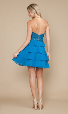 A woman, facing away, wears the Strapless Short Ruffled Hoco Dress: Poly USA 9838—featuring a strapless corset-style lace bodice and layered ruffle skirt—paired with nude heels, set against a beige background.