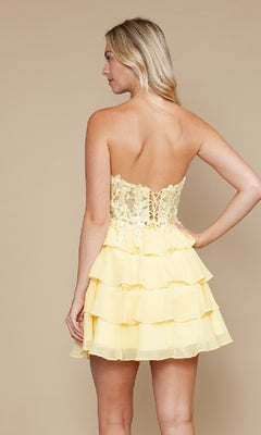 A woman faces away, modeling the Strapless Short Ruffled Hoco Dress: Poly USA 9838, which features a corset-style bodice and tiered ruffle skirt against a plain beige background.
