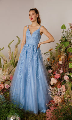 A woman stands among flowers and greenery, wearing the Eureka 9858 Embroidered-Lace Long Prom Dress in light blue with delicate floral appliqué, set against a plain background.