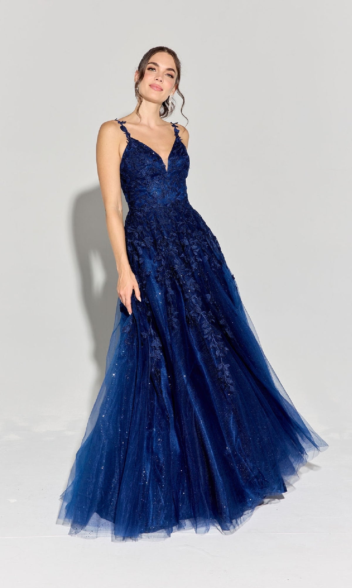 A woman in the Embroidered-Lace Long Prom Dress Eureka 9858, featuring a sleeveless dark blue fitted bodice and full textured skirt, stands against a plain light background.