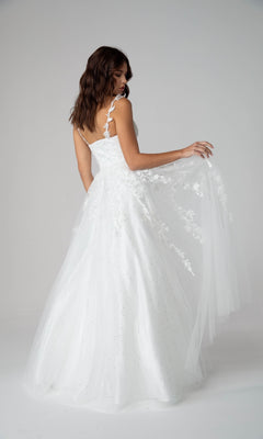 A woman in the Eureka 9858 Embroidered-Lace Long Prom Dress, featuring white floral appliqué details and a sleeveless design, poses against a plain background while holding out part of her skirt.