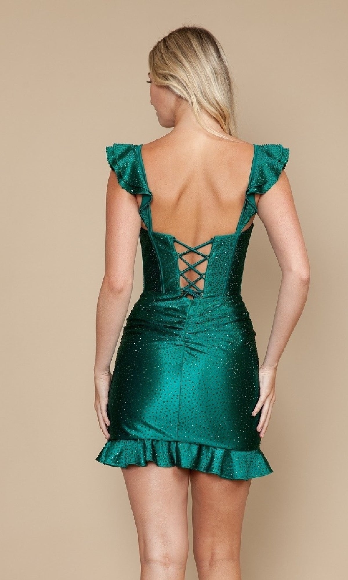 A woman wears the Poly USA 9876 short glitter-satin party dress in emerald green, featuring ruffled sleeves, a ruffled hem, and a chic lace-up back as she stands facing away.