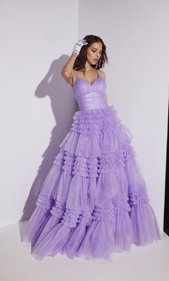 A woman models the Lace-Up Long Glitter-Tulle Prom Dress: Eureka 9888, featuring voluminous lavender tulle, layered ruffles, a sparkling finish, and lace-up back detail as she poses against a white wall with one gloved hand near her head.