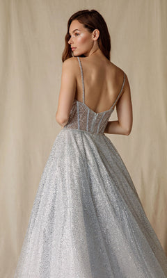 A woman poses against a plain beige backdrop in the Sheer-Corset Glitter Prom Ball Gown: Eureka 9900, a silver, floor-length A-line gown with thin straps, a low back, and sparkling details.