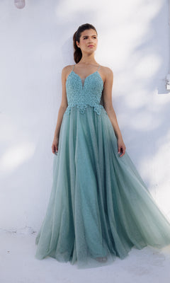 A woman stands against a white wall wearing the Eureka 9901 Lace-Up Long Glitter Prom Ball Gown—a sleeveless light blue dress featuring a fitted lace bodice and a flowing tulle skirt.