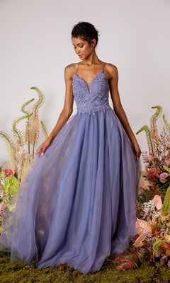 A woman wearing the Lace-Bodice Long Glitter Prom Dress Eureka 9902 with lavender lace, tulle skirt, and spaghetti straps stands amid assorted flowers and greenery.