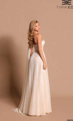 A woman in the Long Formal Dress: Tarik Ediz 99098, a strapless, floor-length ivory gown, stands against a beige background and looks over her shoulder.