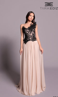 A woman poses against a plain light grey background wearing the Tarik Ediz 99101 long formal dress in pearl, featuring a chiffon A-line skirt and black lace-fitted bodice.