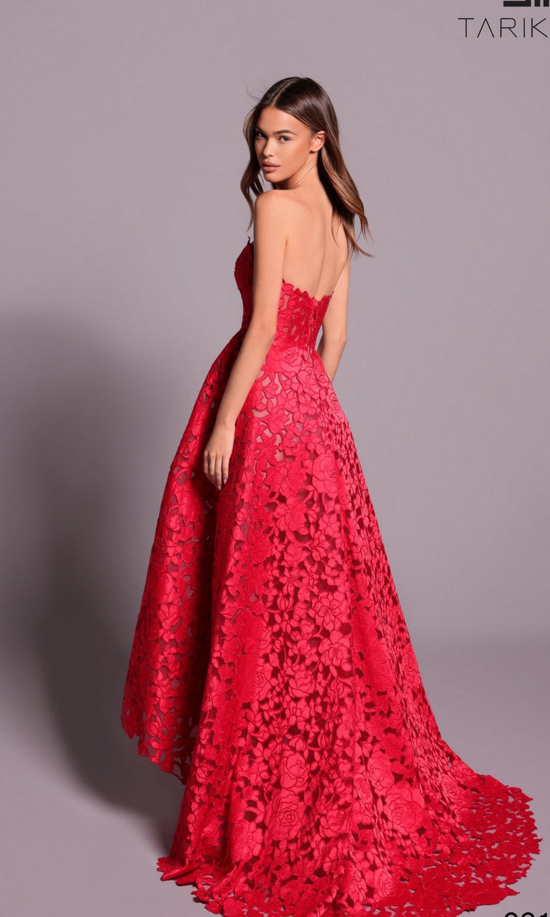 A woman models the Tarik Ediz 99111, a stunning floor-length, strapless formal dress with red floral lace, posed against a plain light background—an elegant pick for special occasions.