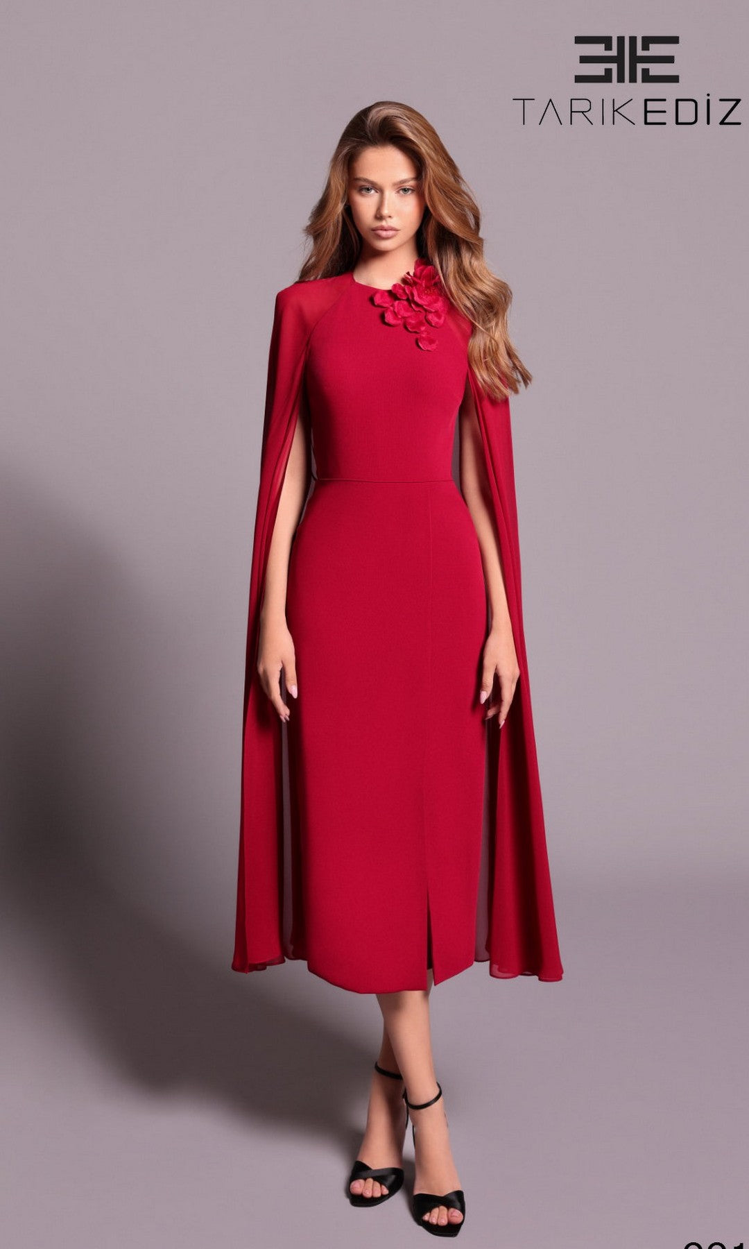 A woman in a dark red Long Formal Dress (Tarik Ediz 99115) with cape sleeves and floral shoulder detailing stands against a plain background. The TARIK EDIZ logo appears in the top right corner.