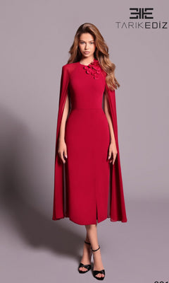 A woman in a dark red Long Formal Dress (Tarik Ediz 99115) with cape sleeves and floral shoulder detailing stands against a plain background. The TARIK EDIZ logo appears in the top right corner.