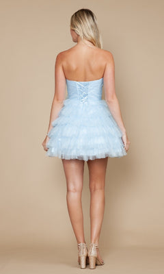 A blonde woman models the Strapless Short Tulle Hoco Dress: Poly USA 9912—a light blue, layered mini dress with ruffles and lace-up back—while posing against a beige background.