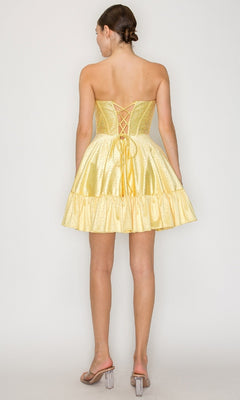A woman stands facing away from the camera in the Poly USA 9942 short homecoming dress, featuring a strapless design, lace-up back, and ruffled hem.