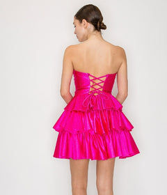 A woman faces away, wearing the Poly USA 9944 short homecoming dress in bright pink, featuring a strapless neckline, tiered layers, and a lace-up back.