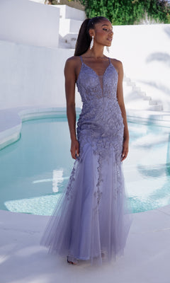 A woman stands by a pool outdoors wearing the Eureka 9958 Embroidered-Lace Long Prom Dress, a lavender gown with strappy back and floral embellishments.