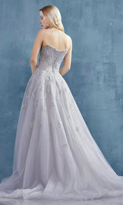 A woman wears the Constellation-Print Strapless Prom Ball Gown A0890, featuring a fitted bodice and flowing tulle skirt, as she stands facing a textured blue wall.