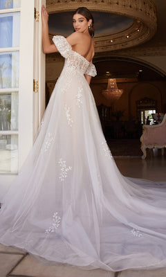 A woman wearing the Puff-Sleeve Long White Wedding Dress A1014, featuring floral lace details and removable puff sleeves, stands by an open door in an ornate room, glancing back over her shoulder.
