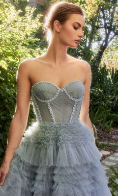 A woman stands outdoors in a Strapless Tiered Long Prom Ball Gown A1017, surrounded by greenery as sunlight highlights her light blue ruffled tulle dress.