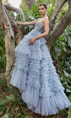 A woman in the Strapless Tiered Long Prom Ball Gown A1017 with ruffled tulle stands by a tree in a lush, green outdoor setting.