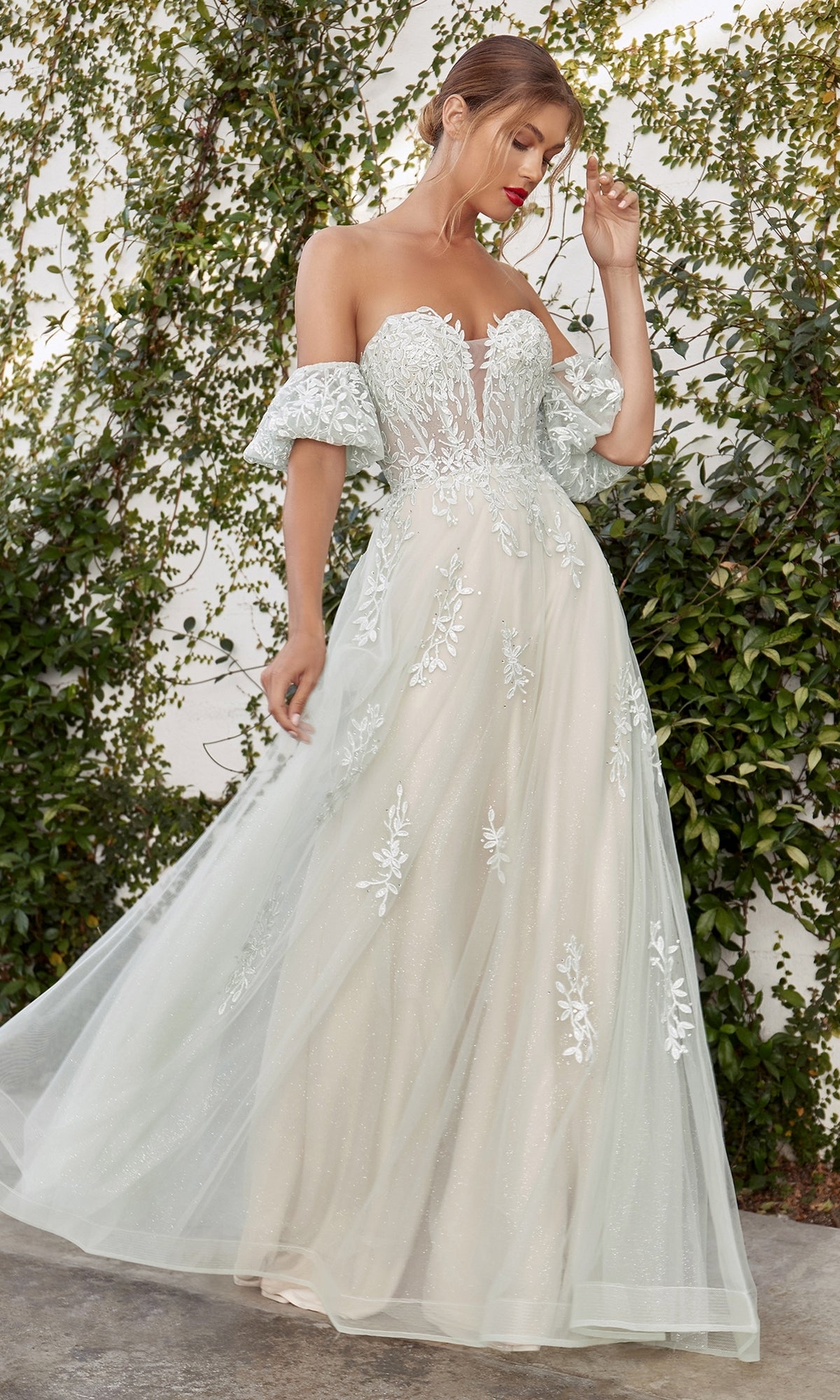 A woman stands outdoors before a leafy green wall, wearing the Strapless Puff-Sleeve Long Prom Ball Gown A1046, a white dress featuring sparkly embroidered floral details and puff sleeves.