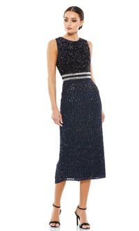 Woman in the Mac Duggal 10509 Short Sequin Wedding Guest Dress, sleeveless and dark blue with a silver waistband, paired with black high-heeled sandals, stands against a white background.
