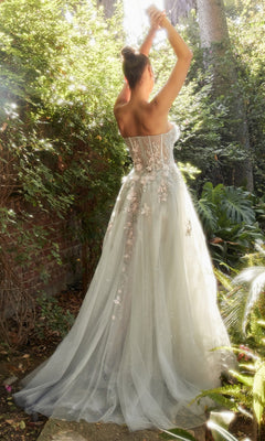 A woman stands outdoors in a garden, arms raised and facing away, wearing the Strapless Sweetheart Floral Prom Ball Gown A1089.