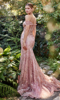 A woman wears the Off-Shoulder Long Sequin Mermaid Prom Dress A1107, a fitted pink gown shimmering among lush green foliage as she stands outdoors on a stone path.