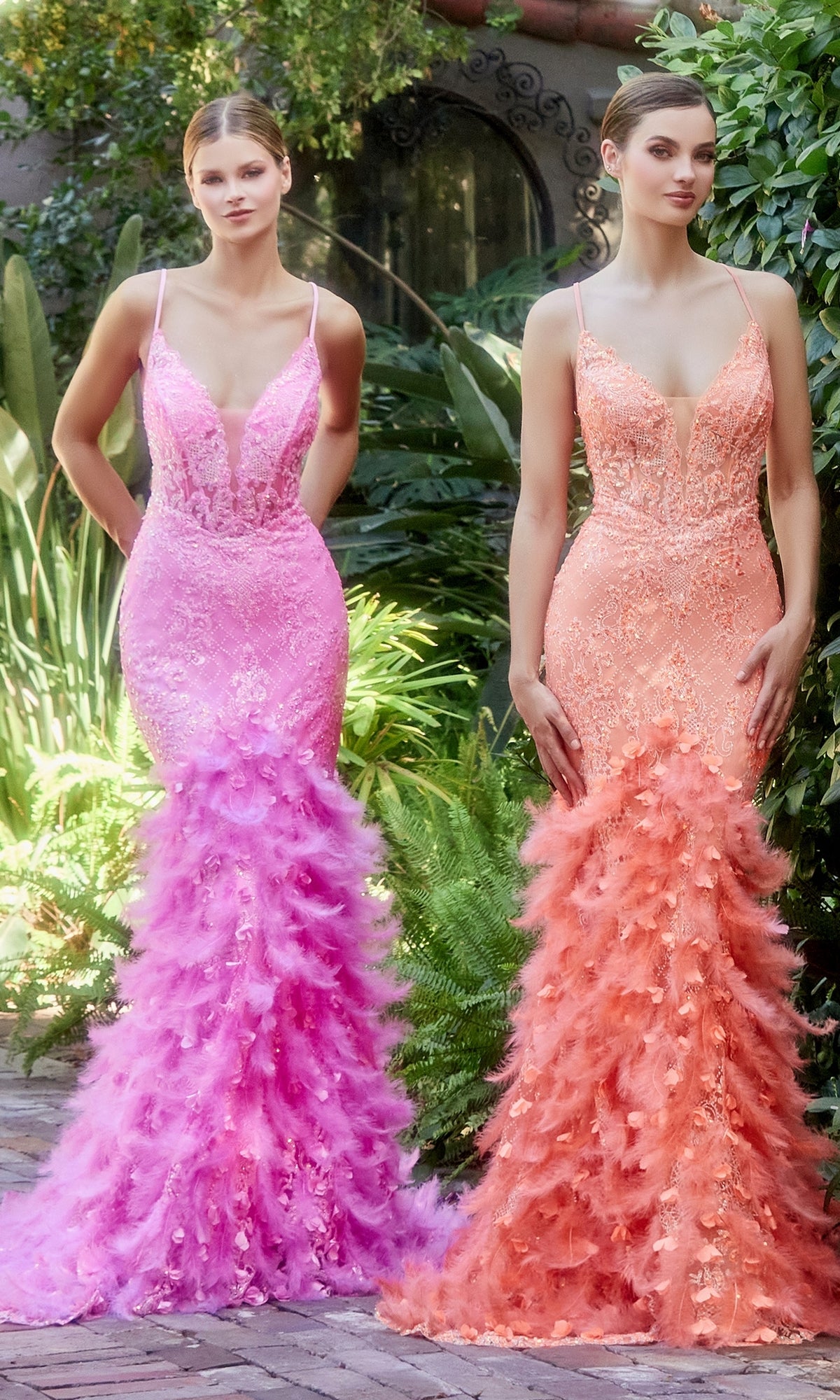 Two women stand outdoors in Long Mermaid Formal Gown with Feathers A1116—one in pink, one in peach. The form-fitting dresses feature deep necklines and feathered skirts, their elegance set off by the lush greenery around them.
