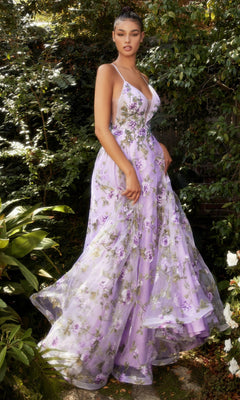 A woman stands outdoors in lush greenery wearing the Lilac Purple Floral-Print Long Prom Dress A1135, featuring a flowing skirt, fitted bodice, and thin straps.