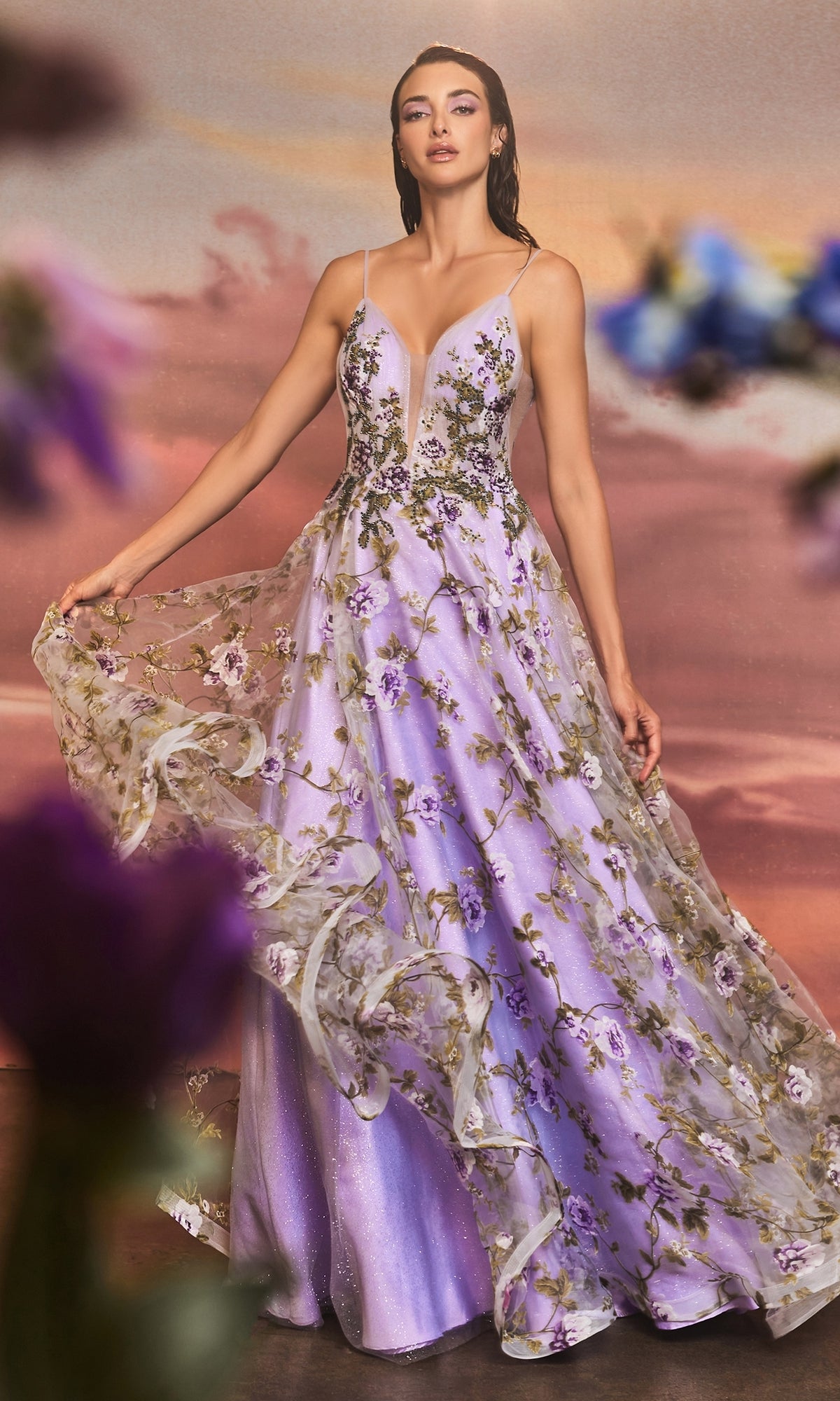 A woman poses in the Lilac Purple Floral-Print Long Prom Dress A1135, featuring spaghetti straps and a deep V-neck, against a soft, sunset-colored background.