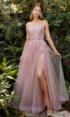 A woman stands outdoors in lush greenery wearing the Butterfly Sheer-Bodice Prom Ball Gown A1141—a sleeveless pink tulle dress with delicate floral embroidery and a thigh-high slit.