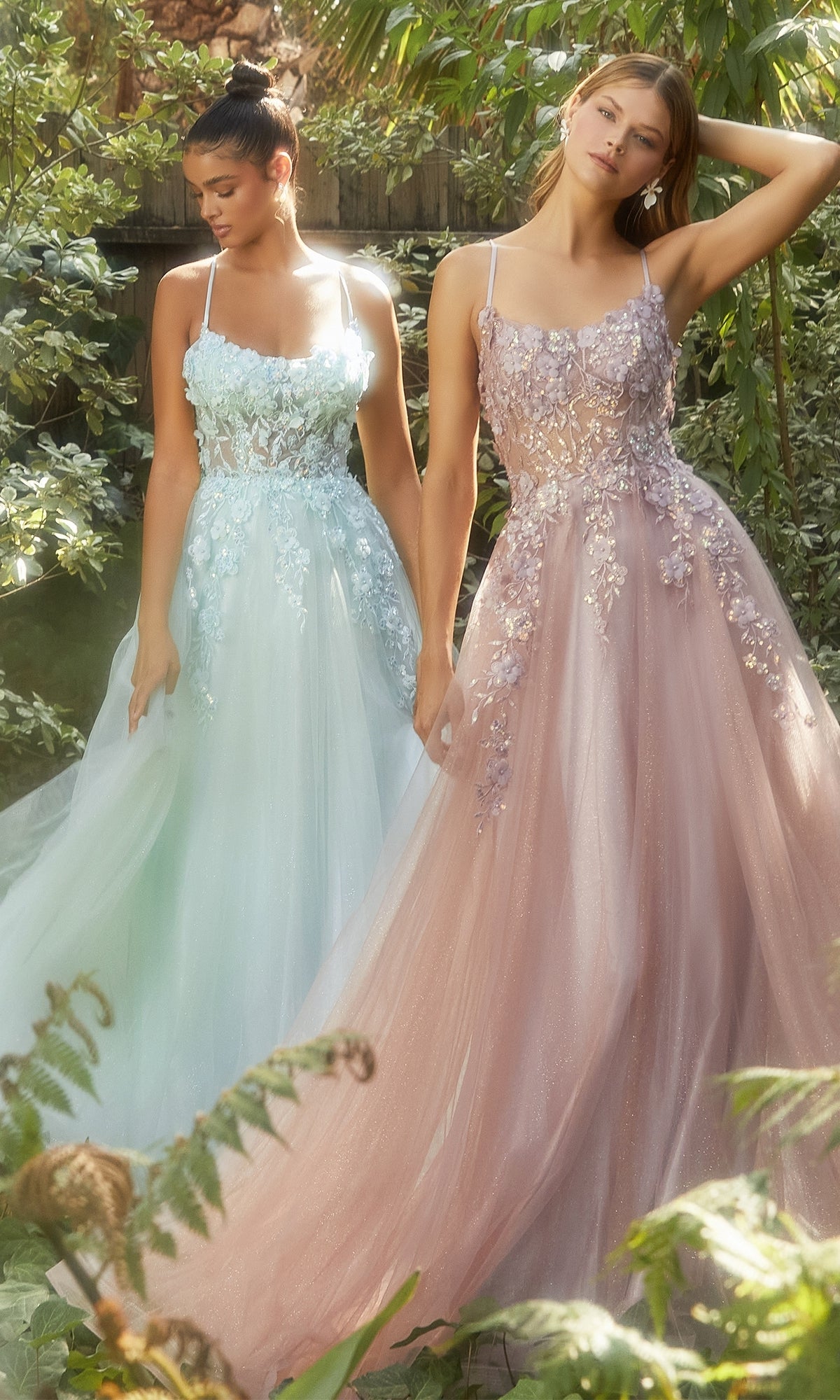 Two women stand outdoors in Flower-Embellished Long Tulle Prom Ball Gown A1142, showcasing pastel, floor-length gowns with sheer waists and delicate 3D floral details amid lush greenery.